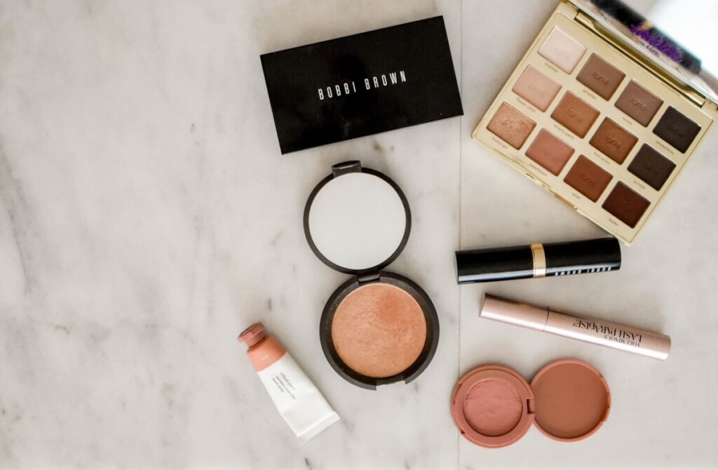 Makeup flatlay featuring luxury and dupe products on a marble surface