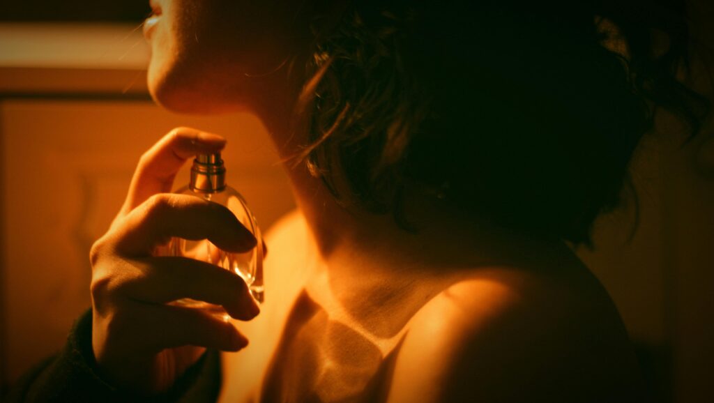 Artistic close-up of a woman applying perfume with warm lighting.