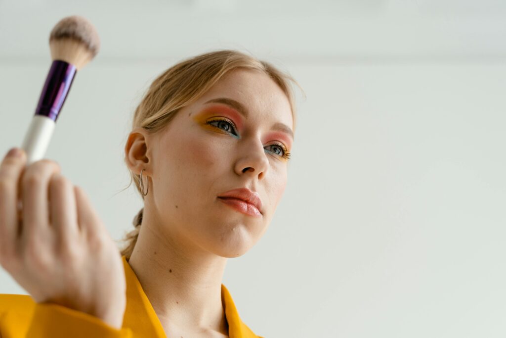 Close-up of woman applying vibrant makeup with a brush, featuring colorful eyeshadow.