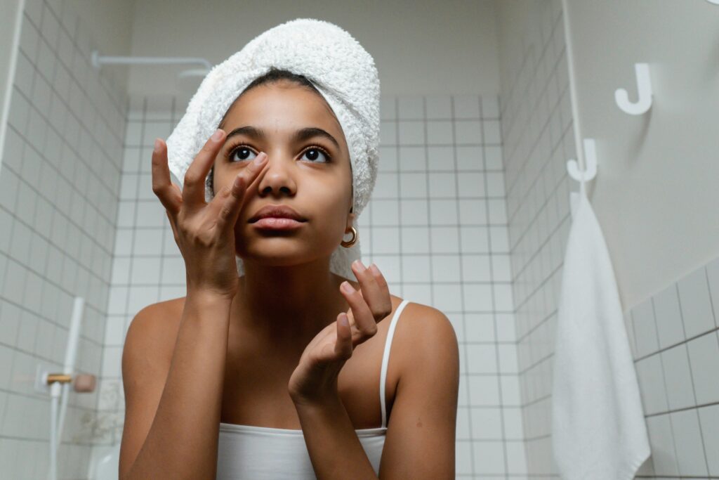A young woman applies skincare in a tiled bathroom, promoting healthy skin routines.