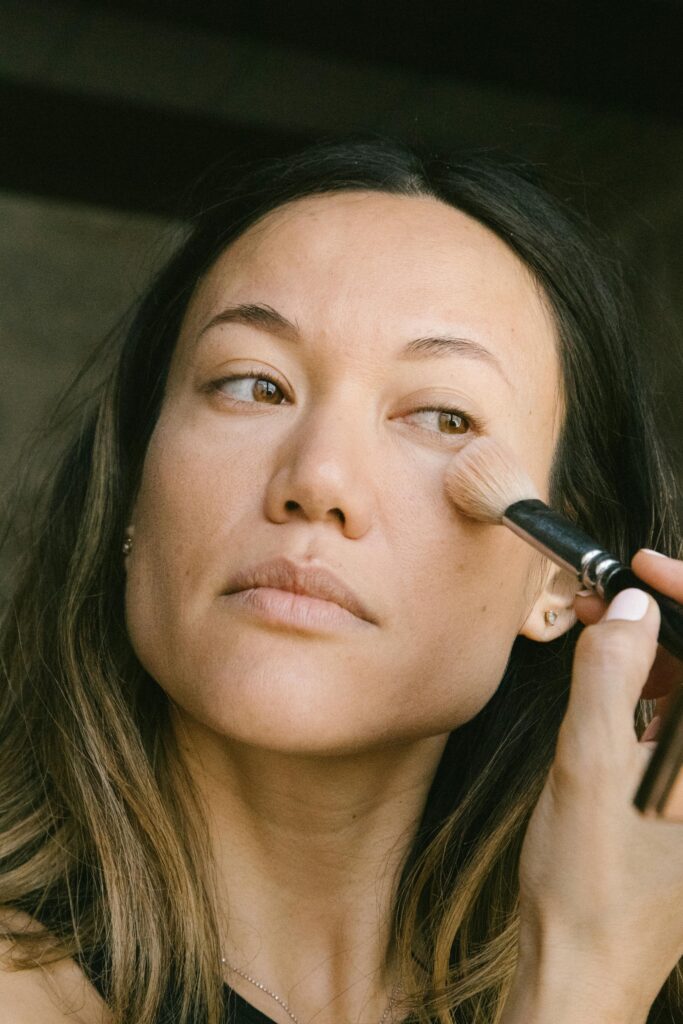 Woman gently applying makeup with a brush to her face indoors.