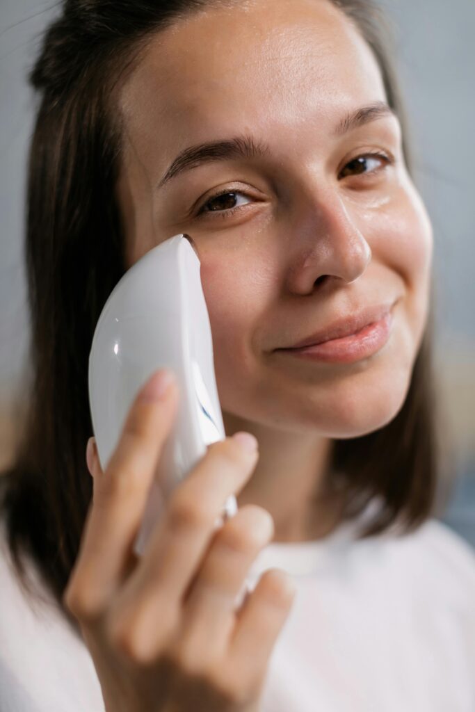 A close-up of a smiling woman using a facial skincare device indoors for healthy skin.